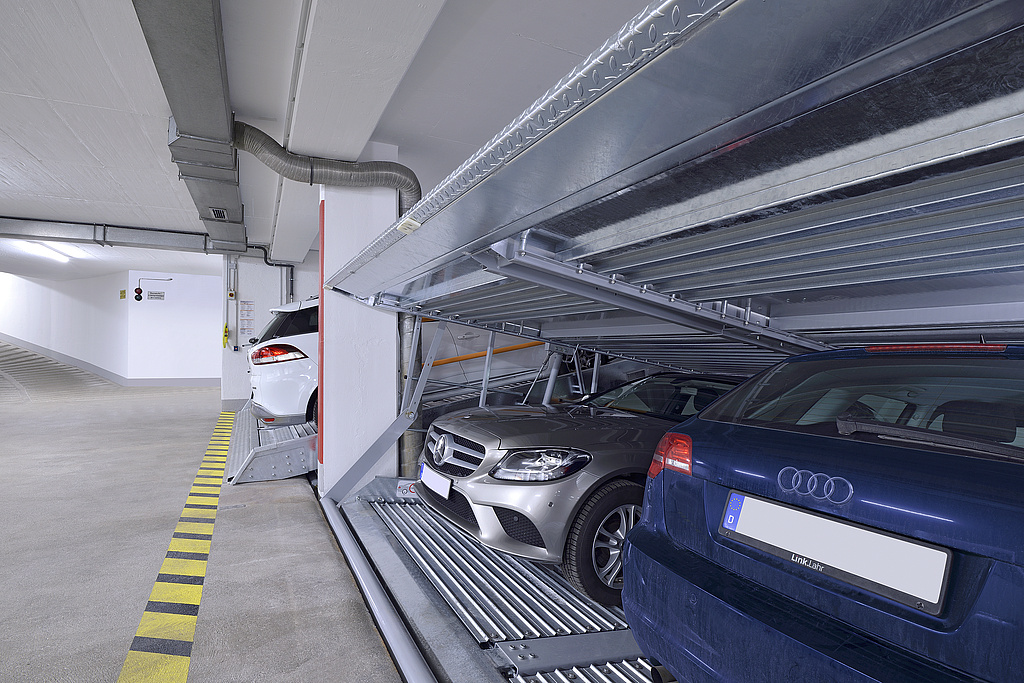 Eine Tiefgarage mit Parksystemen im Vordergrund, in denen mehrere Autos stehen