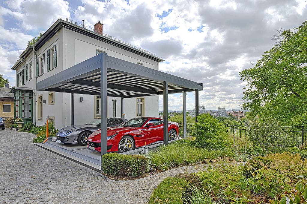 Seitenansicht des Carport und Parksystem, mit 2 Autos. Im Hintergrund das Anwesen