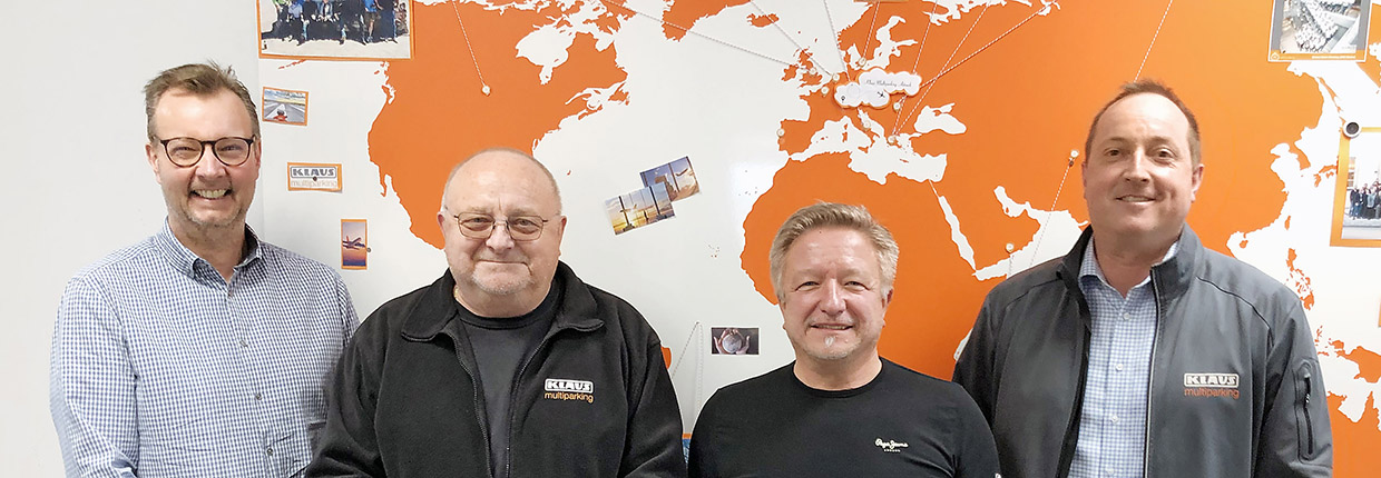 Vier Männer schauen nach vorne, im Hintergrund eine Weltkarte in orange